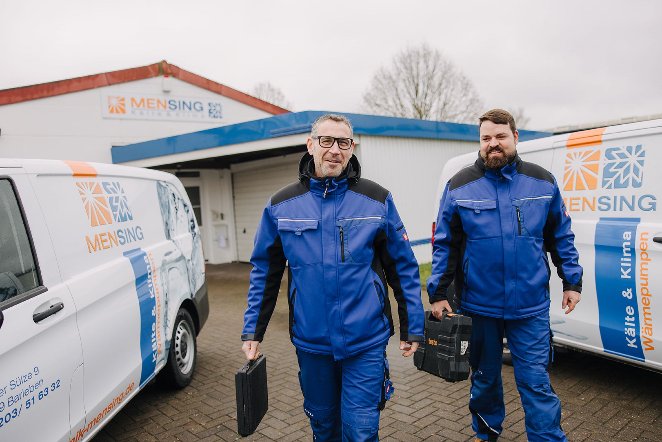 Mensing Kälte & Klima Techniker mit Werkzeug vor Servicefahrzeugen – Experten für Kältetechnik und Wärmepumpen.